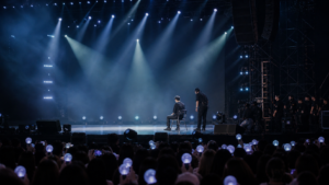 Generic K-pop concert stage pause with a seated performer and staff nearby