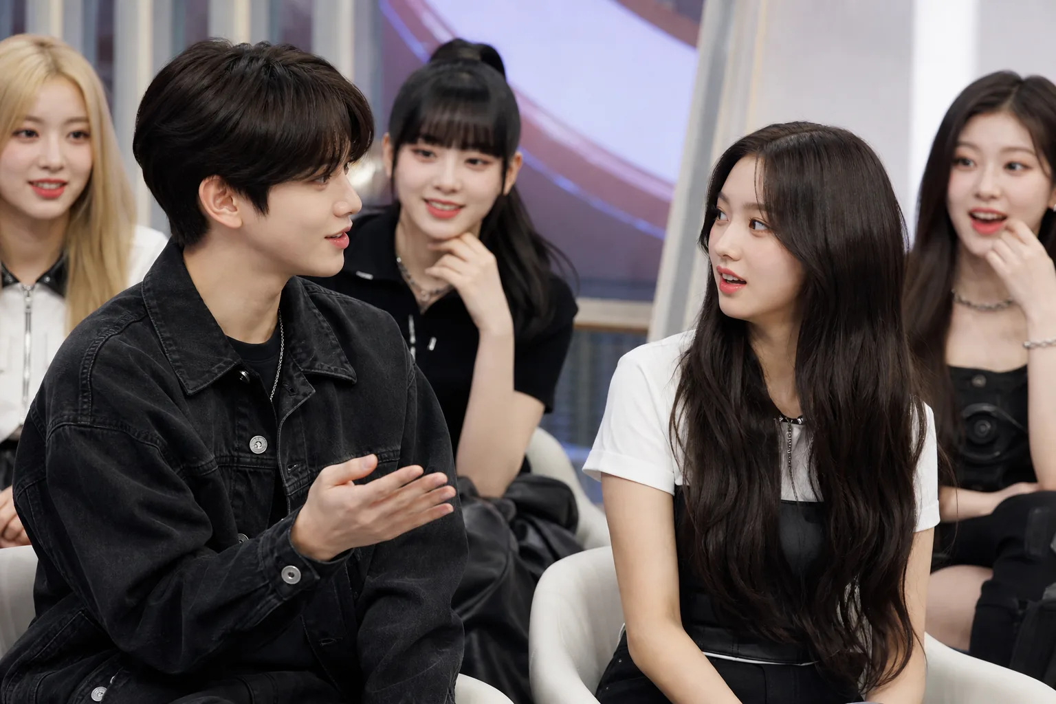 K-pop idols filming a studio variety show segment with a friendly discussion