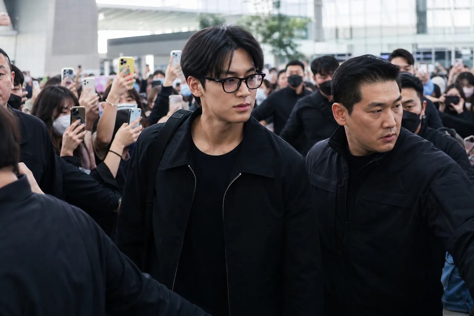 K-pop idol moving through a crowded airport with security nearby