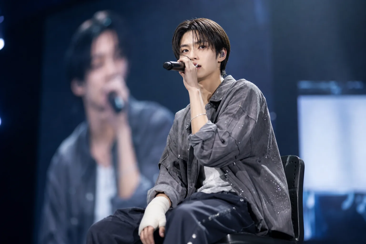 K-pop performer seated on stage after hand injury