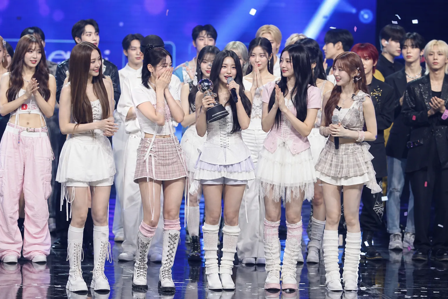 Modern K-pop stage with performers and broadcast lighting