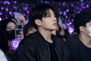 K-pop concert crowd with bright stage lights as fans film a surprise celebrity sighting