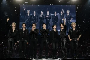 A K-pop boy group performing under concert lights in a large arena