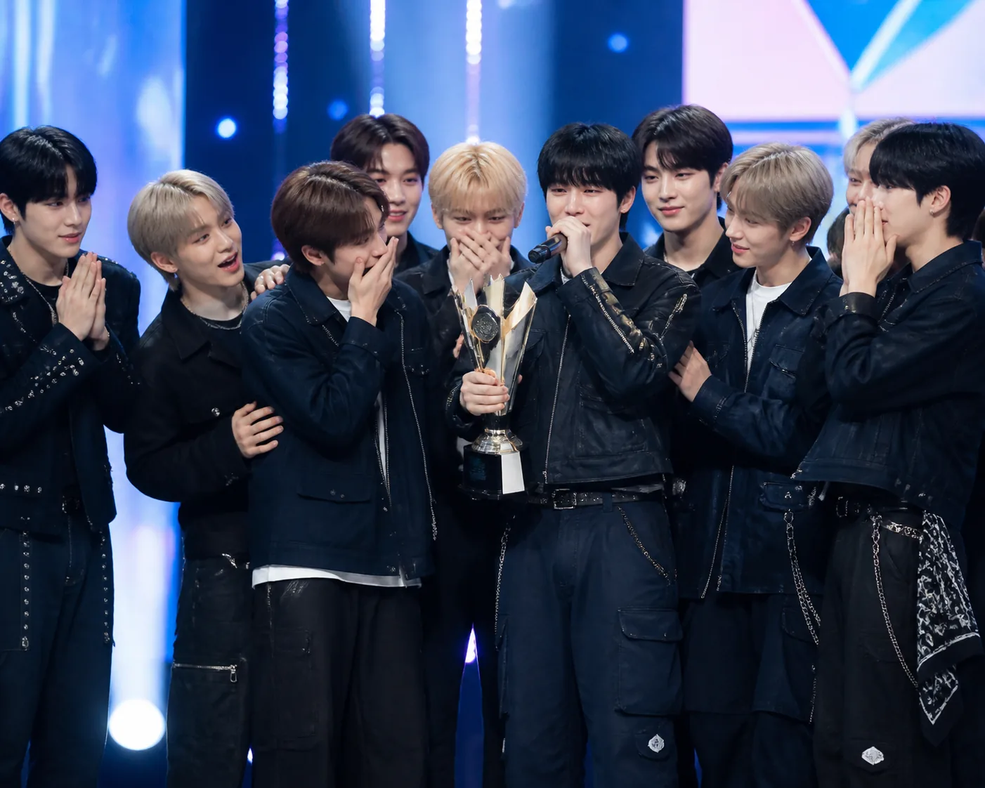 K-pop performers holding a trophy under concert lights