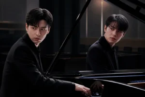Two young pianists performing together at a grand piano in a rehearsal room
