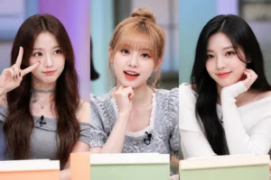 Three K-pop performers in a colorful television variety-show studio