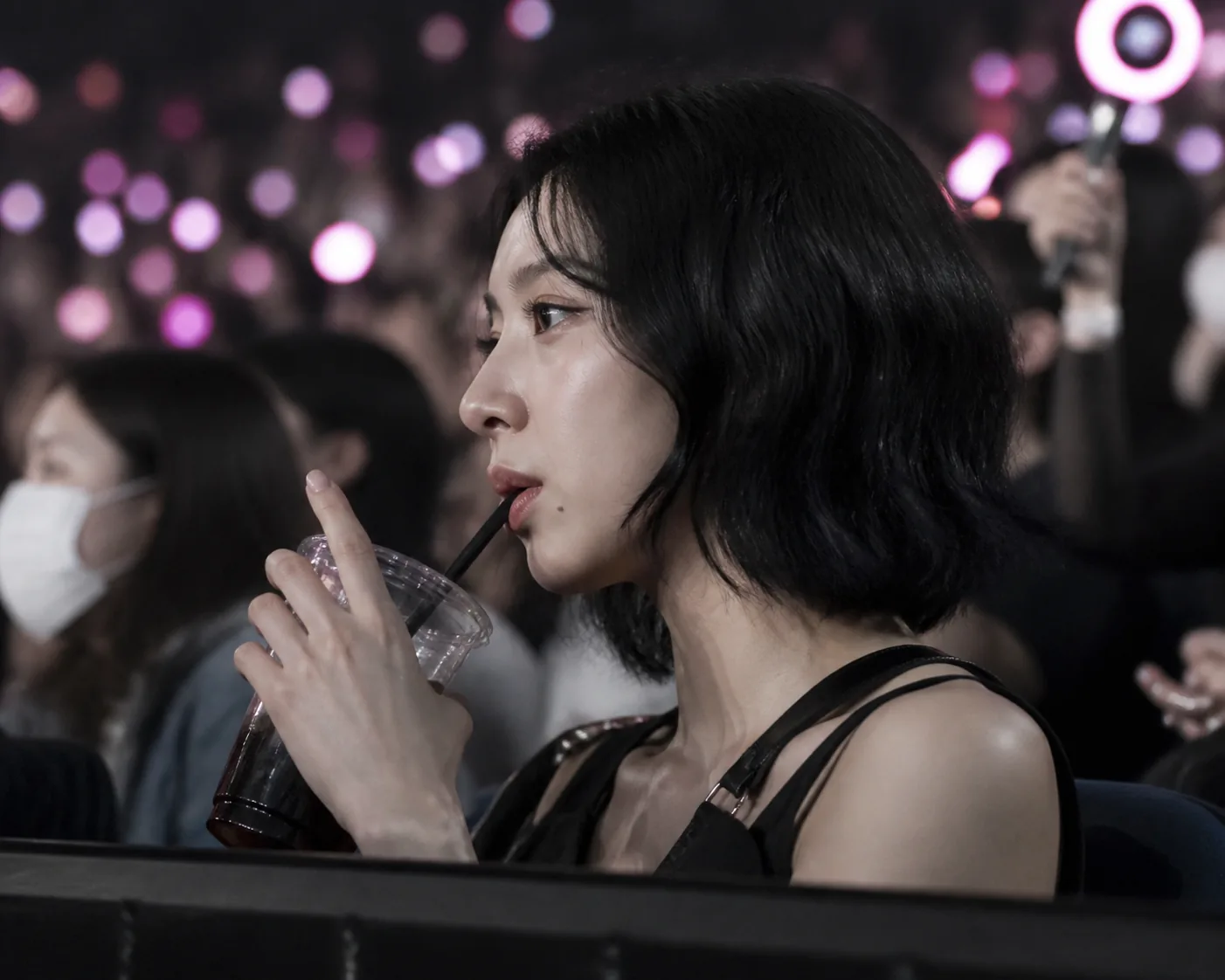 Concertgoer holding a drink in dim lighting while a phone records nearby