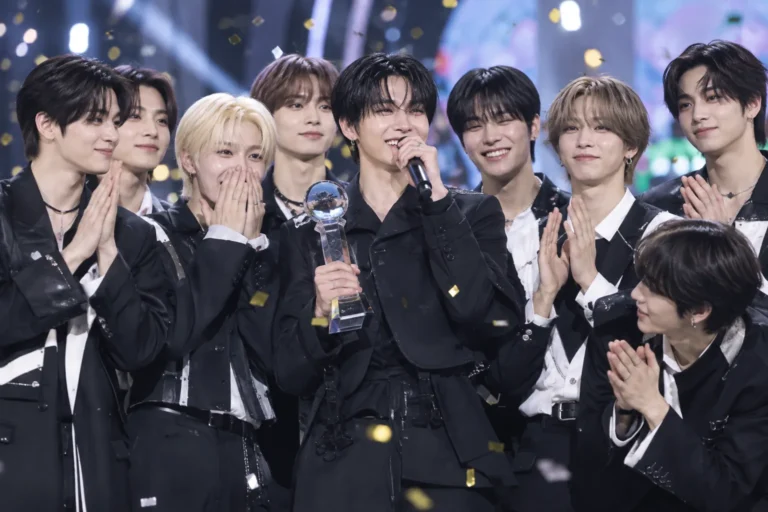 K-pop group celebrating a music show trophy on a bright television stage